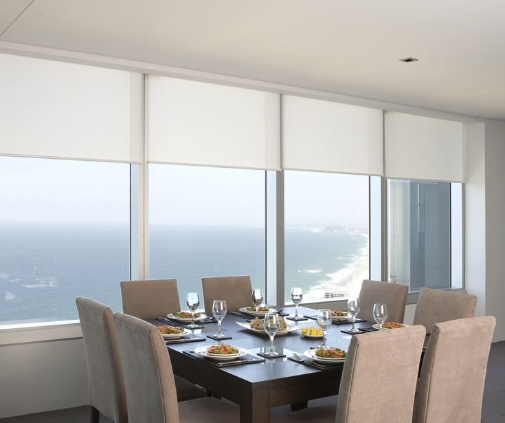 Elegant dining area with large windows covered with sheer white Roller/Holland Blinds filtering sunlight into the space.